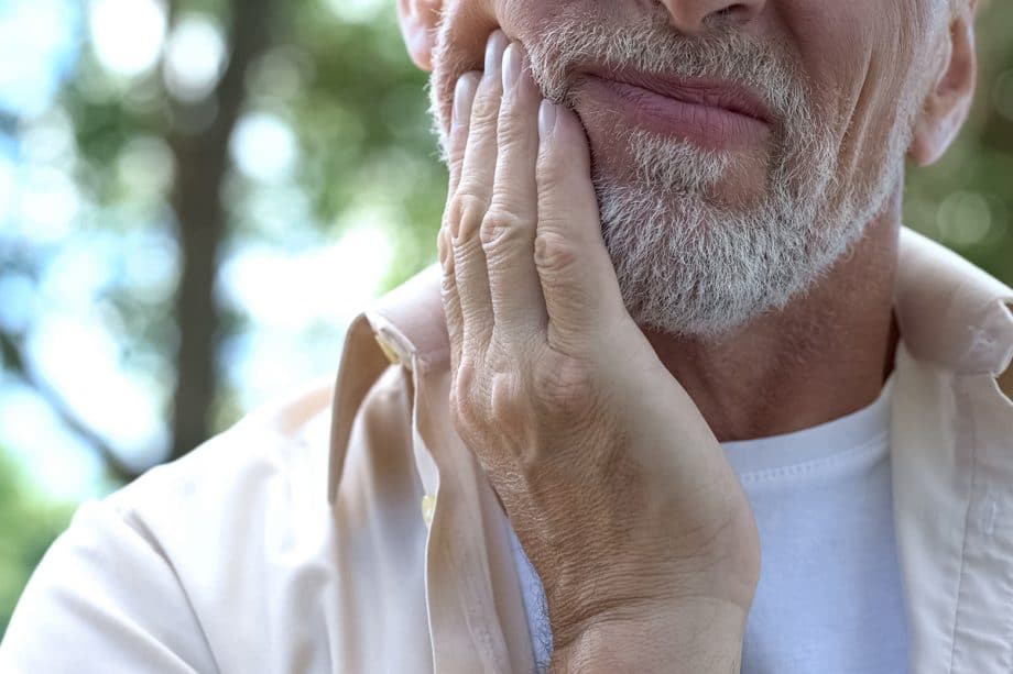 a bearded man touches his jaw in pain